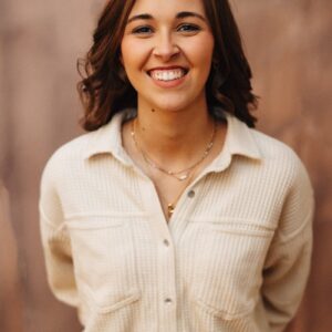 A smiling woman poses in front of a wall.